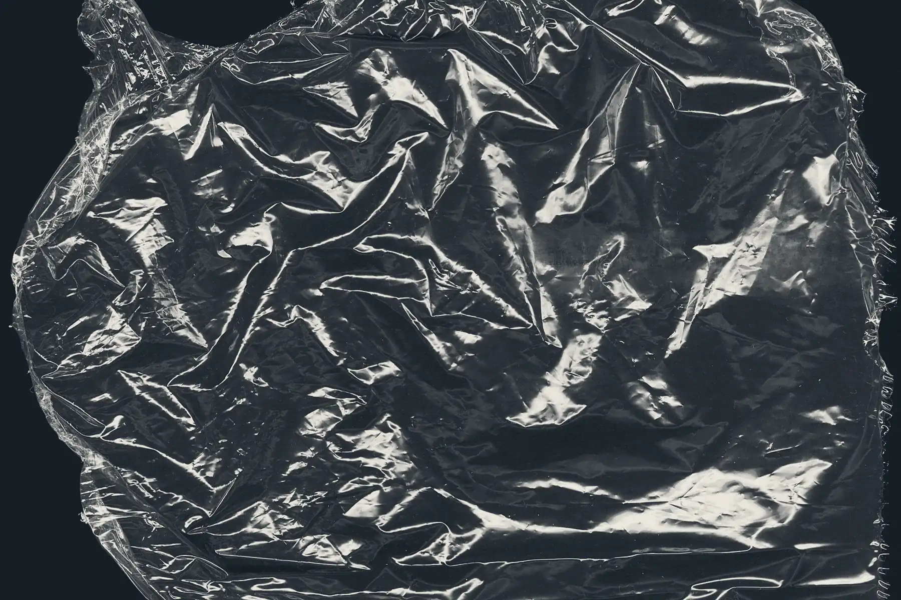 A single discrete sheet of clear packaging film on a dark ground, one torn boundary and a folded gusset legible across it.